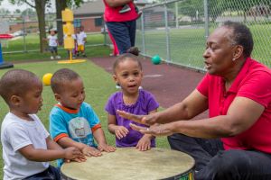 Teacher and children playing muisc on a large drum.