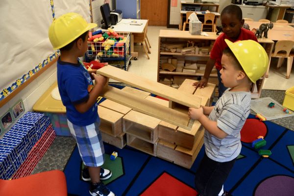 Two boys wearing toy construction helmets while placing long planks of wood into place.