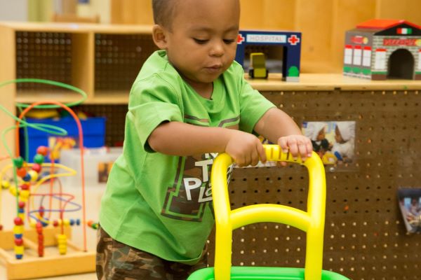 Child playing with a toy wheeled cart.